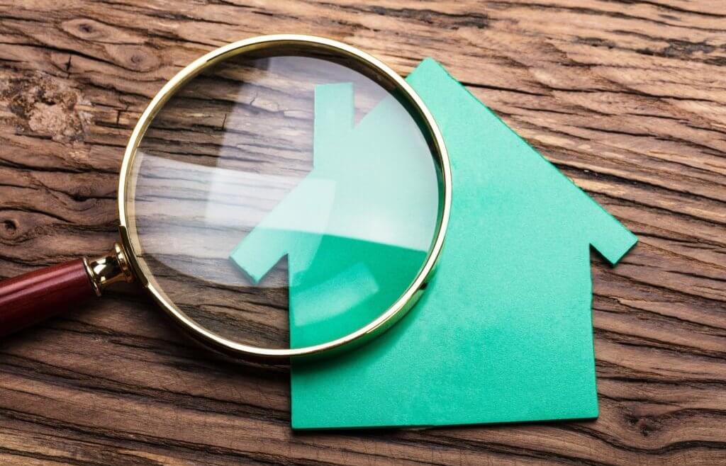 Magnifying glass on top of a green paper home laying on a wooden background