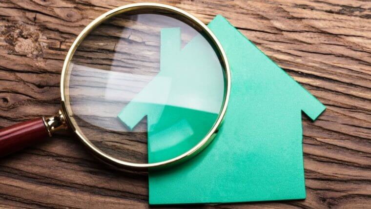 Magnifying glass on top of a green paper home laying on a wooden background